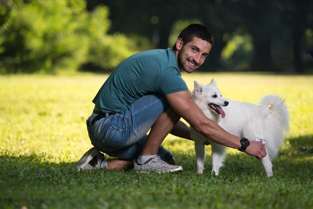 公園で犬のジャーマンスピッツと一緒に座っている若い男彼は彼をきれいにします