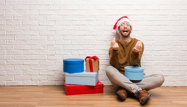 Giovane che si siede con i regali che celebrano il natale facendo un gesto di bisogno