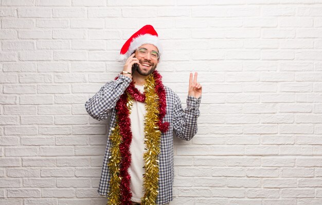 勝利のジェスチャーをしてクリスマスを祝う贈り物と一緒に座っている若い男