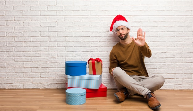 Young man sitting with gifts celebrating christmas putting hand in front