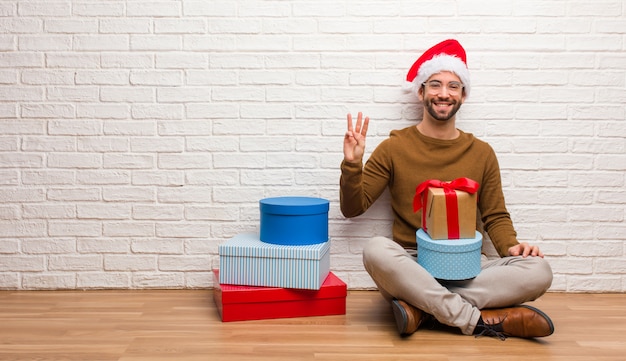 Young man sitting with gifts celebrating christmas showing number three