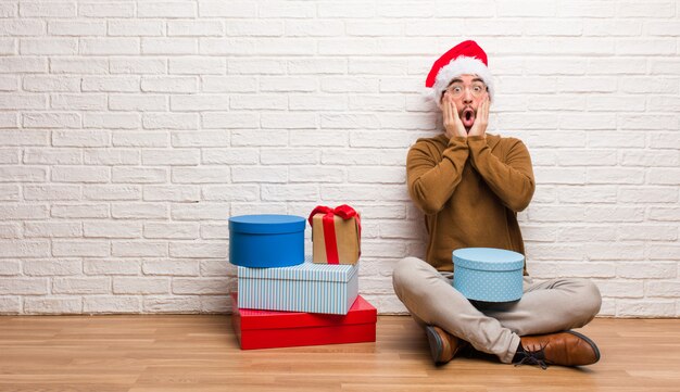 Молодой человек, сидящий с подарками, празднующими рождество, удивлен и потрясен