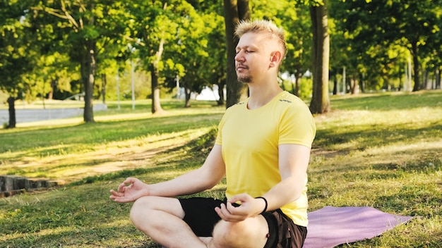 Young man sitting on a yoga mat in Lotus position preparing to practice yoga and meditation outdoors Fitness and healthy concept