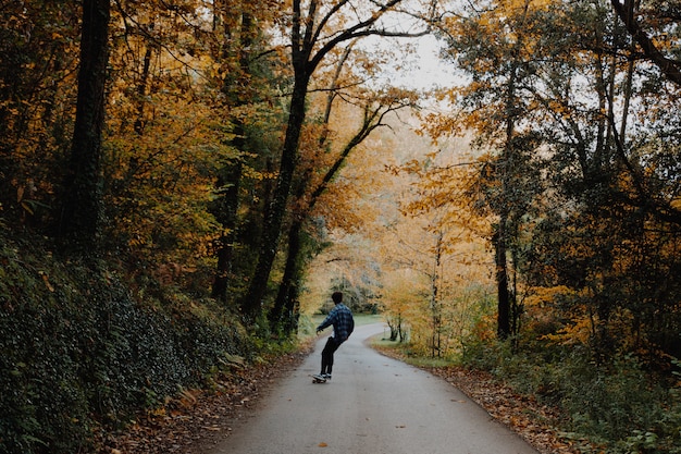 Skateboarding del giovane nel mezzo della foresta in autunno in catalogna