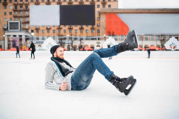 Photo young man in skates sitting on ice, skating rink