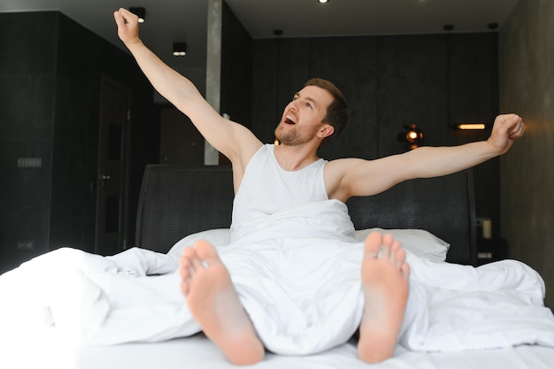 Young man sleeping waking up and stretching in his bed