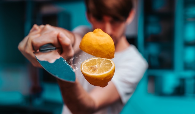 Photo young man slicing with sharp knife a flying juicy fresh lemon