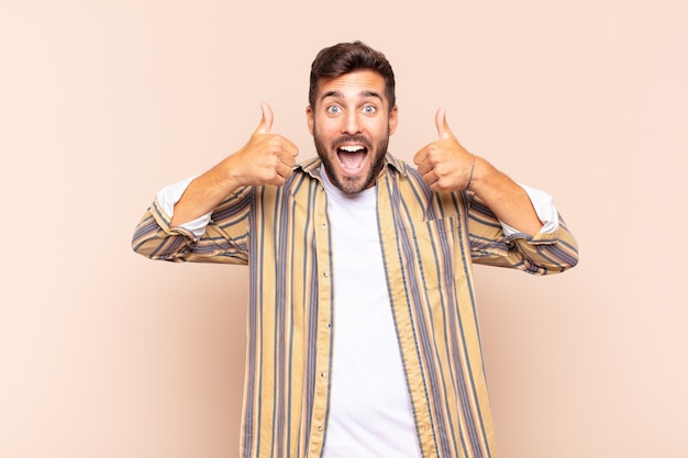 Young man smiling broadly looking happy, positive, confident and successful, with both thumbs up