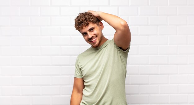 Young man smiling cheerfully and casually, taking hand to head with a positive, happy and confident look