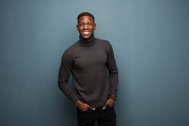 Young man smiling cheerfully and casually with a positive, happy, confident and relaxed expression over grunge wall