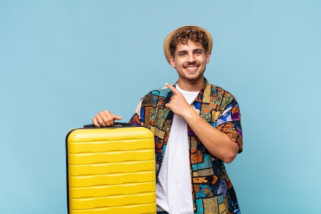 Young man smiling cheerfully, feeling happy and pointing to the side and upwards, showing object in copy space.