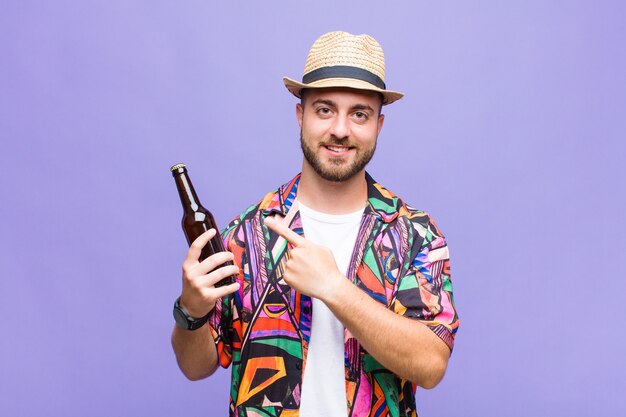 Young man smiling cheerfully, feeling happy and pointing to the side and upwards, showing object in copy space