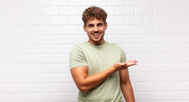 Young man smiling cheerfully, feeling happy and showing a concept in copy space with palm of hand