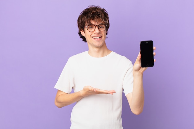 Young man smiling cheerfully, feeling happy and showing a concept and holding a cell