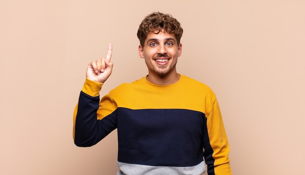 Young man smiling cheerfully and happily, pointing upwards isolated