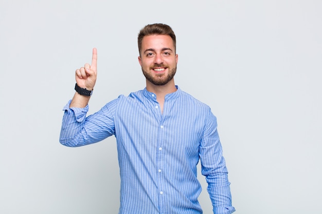 Young man smiling cheerfully and happily, pointing upwards with one hand to copy space