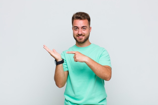 Young man smiling cheerfully and pointing to copy space on palm on the side, showing or advertising an object