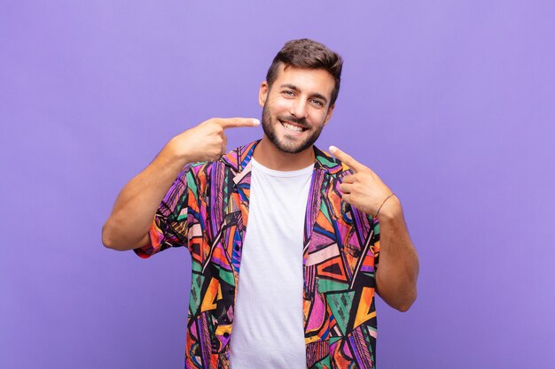 Young man smiling confidently pointing to own broad smile, positive, relaxed, satisfied attitude