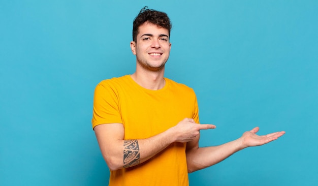 Young man smiling, feeling happy, carefree and satisfied, pointing to concept or idea on copy space on the side