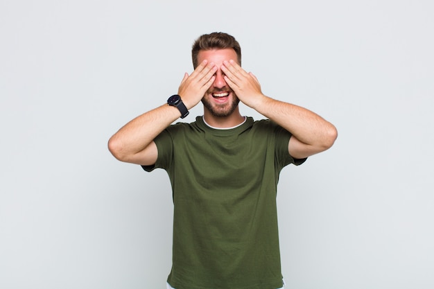 Young man smiling and feeling happy, covering eyes with both hands and waiting for unbelievable surprise