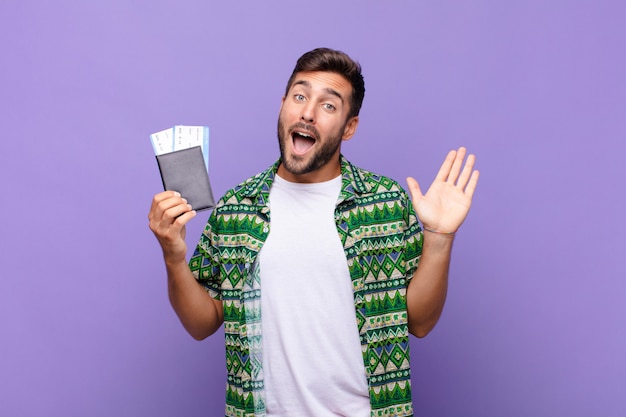 Young man smiling happily and cheerfully, waving hand, welcoming and greeting you, or saying goodbye