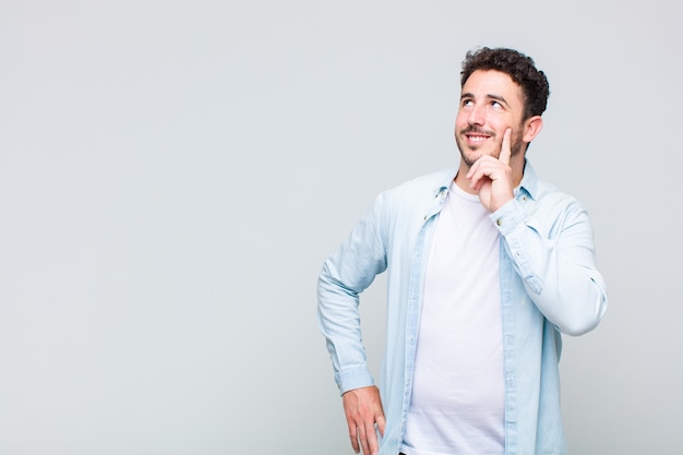 Giovane uomo sorridente felicemente e fantasticando o dubitando, guardando al lato