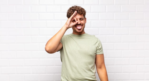 Young man smiling happily with funny face, joking and looking through peephole, spying on secrets