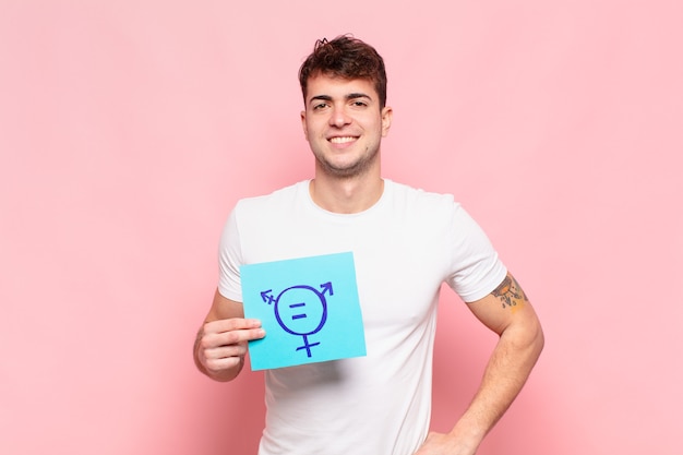 Young man smiling happily with a hand on hip and confident, positive, proud and friendly attitude