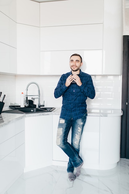 Young man smiling and holding coffee at home in the kitchen