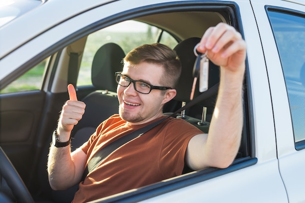 Young man smiling and holding key in his car. Auto purchase and people concept