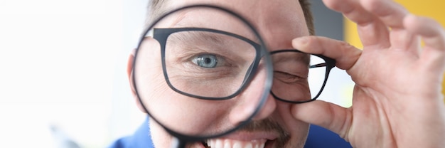 Photo young man smiling and holding magnifying glass in front of his eyes closeup error  concept