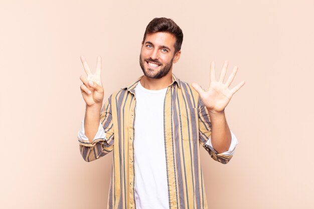 Young man smiling and looking friendly, showing number seven or seventh with hand forward, counting down