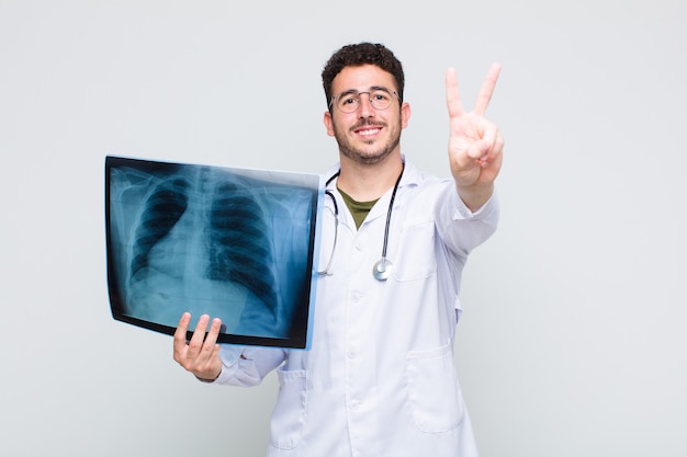 Young man smiling and looking happy, carefree and positive, gesturing victory or peace with one hand