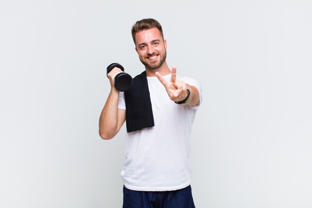 Young man smiling and looking happy, carefree and positive, gesturing victory or peace with one hand