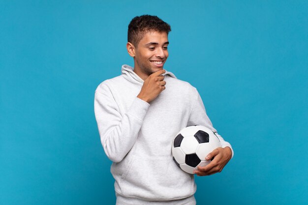 Young man smiling with a happy, confident expression with hand on chin, wondering and looking to the side. soccer concept