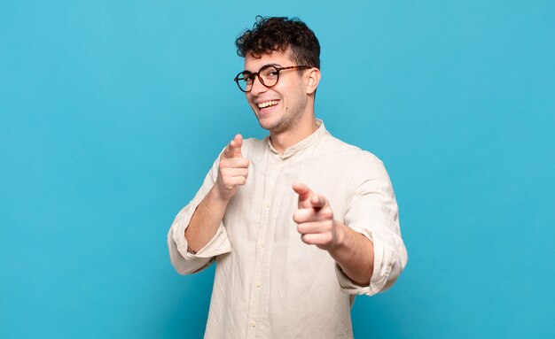 Young man smiling with a positive, successful, happy attitude pointing , making gun sign with hands