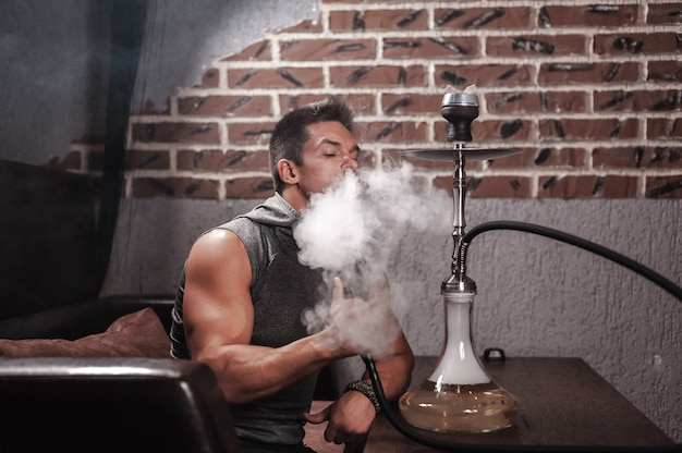 Young man smokes a fragrant oriental hookah at the bar