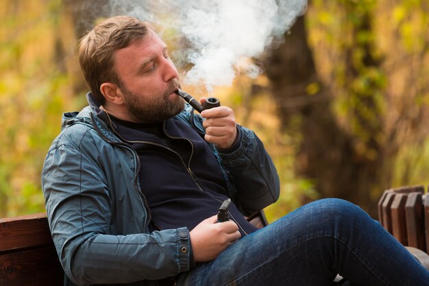 Young man smokes tobacco pipe in park