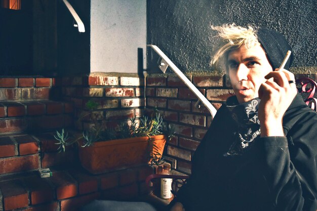 Photo young man smoking cigarette against wall at night