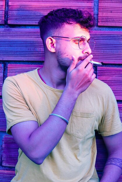 Young man smoking cigarette against wall