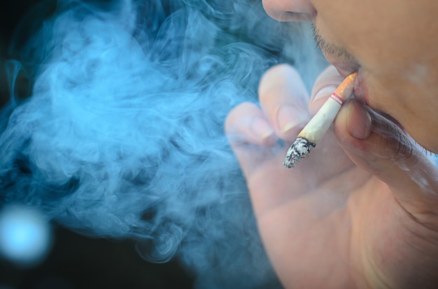 Young man smoking cigarette on black background with smoke