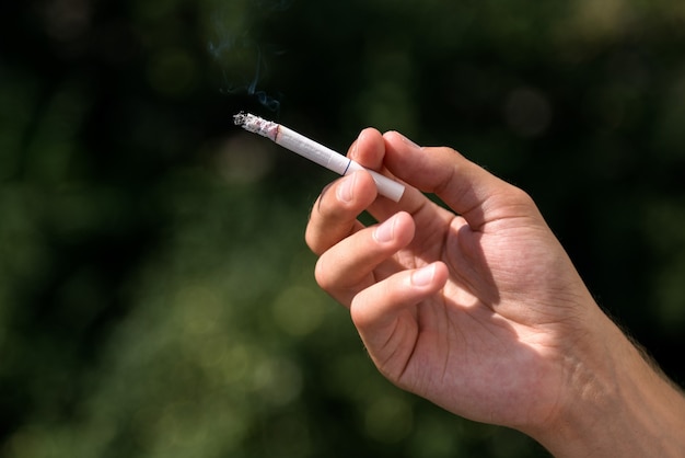 若い男がタバコを吸う、有毒なタバコの煙を吸い込む、喫煙を殺す、警告