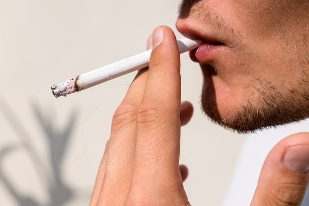 Young man smoking cigarette, inhaling toxic tabacco smoke.