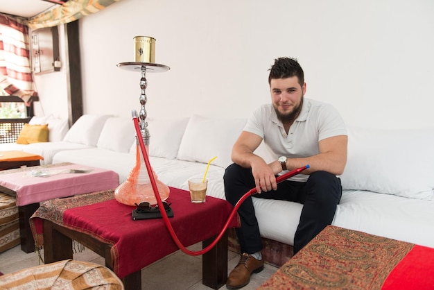 Young man smoking shisha at arabic restaurant man exhaling\
smoke inhaling from a hookah