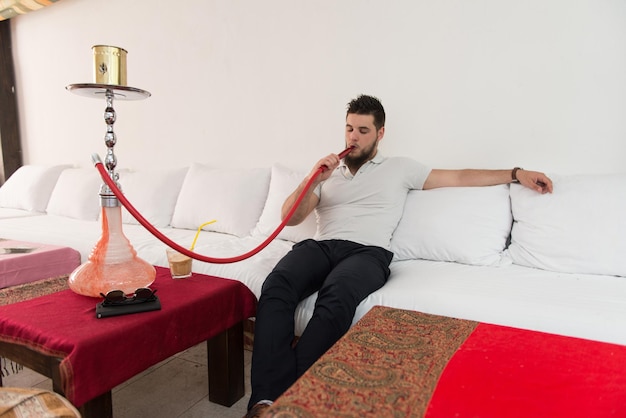 Young man smoking shisha at arabic restaurant man exhaling
smoke inhaling from a hookah