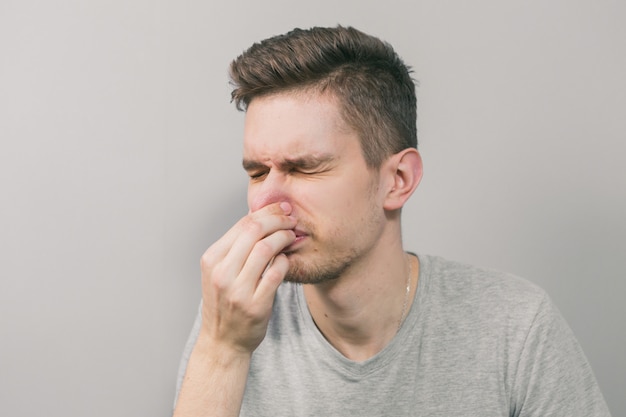 Young man sneezes in hand on gray background