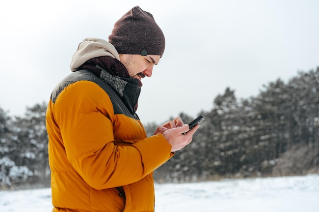 Young man in snowy winter forest using cell phone