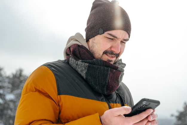 携帯電話を使用して雪の冬の森の若い男