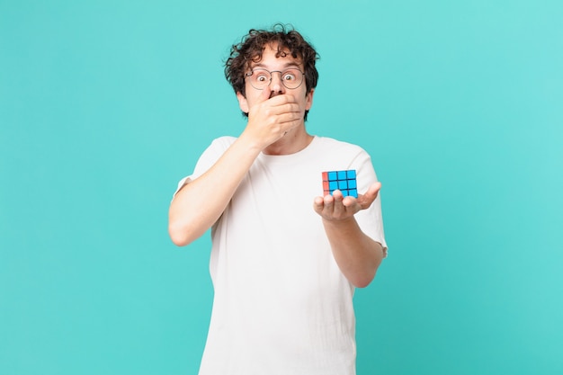 Young man solving an intelligence problem covering mouth with hands with a shocked