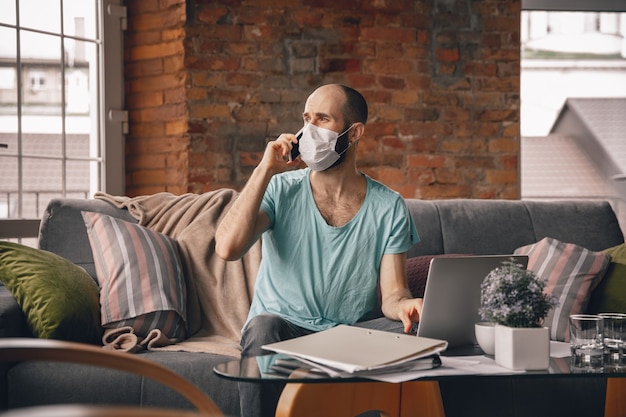 Photo young man speaking on the phone at home while being quarantine and freelance working